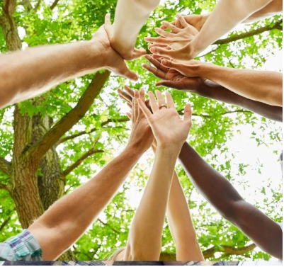 Un grupo de personas levantando sus manos hacia el cielo en un ambiente al aire libre, rodeados de árboles. La imagen transmite unidad y colaboración en un entorno natural. Grupos de apoyo a familiares. Mayo, 2024