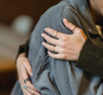 Primer plano de dos personas abrazándose, una con una chaqueta de pana gris y la otra con anillos en los dedos abrazándola.